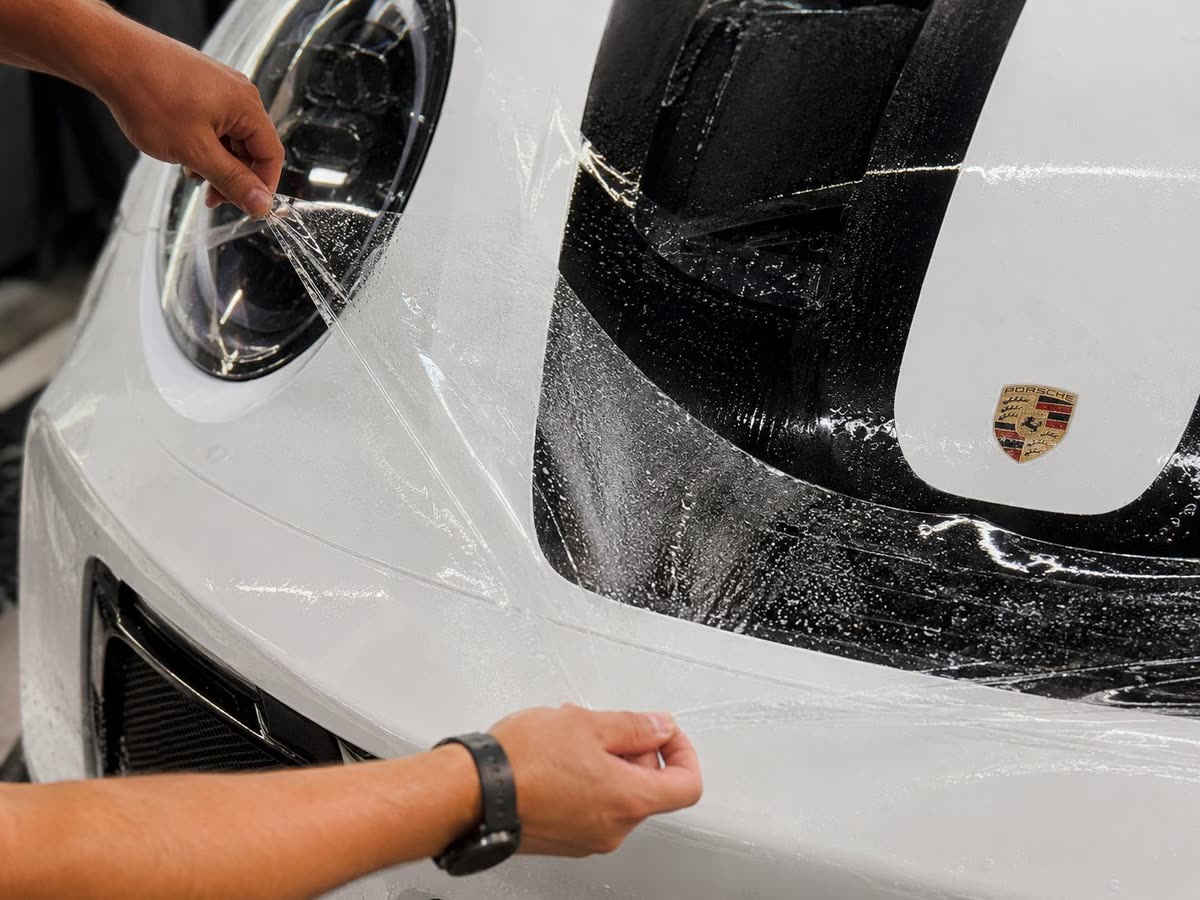 Installer applying clear paint protection film to a white Porsche front bumper
